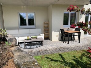 Eine Terrasse mit einem weißen Sofa, einem Holztisch und einem schwarzen Stuhl.