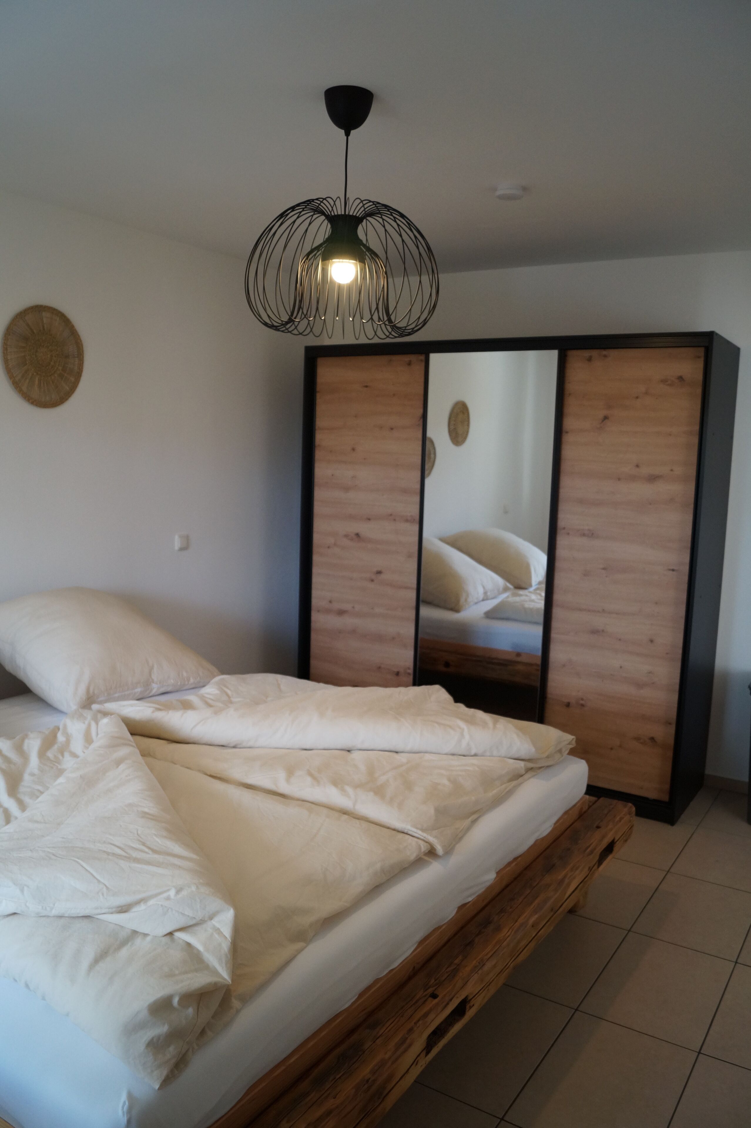 Un dormitorio con cama, cabecera de madera, espejo y lámpara colgante.