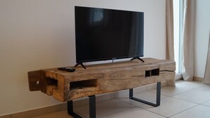 En TV-möbel i trä med en platt-TV, svarta metallben och en fjärrkontroll på vänster sida.
