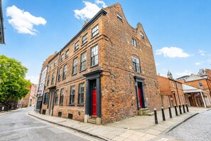 Een historisch bakstenen gebouw met meerdere ramen, een rode deur en een kinderafdekkingsstraat.