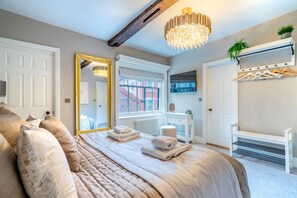 A bedroom with a large bed, a mirror, a chandelier, a radiator, and a television. - Friargate House - a premium stay that sleeps 9 guests in 4 bedrooms (York)
