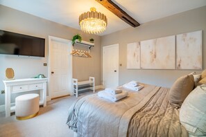 Une chambre à coucher avec un lit, une coiffeuse avec un miroir, une télévision et des œuvres d’art accrochées au mur.
