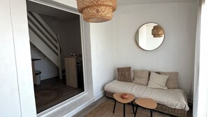 A cozy living room with a sofa, two small tables, a woven floor lamp, and a round mirror on the wall.