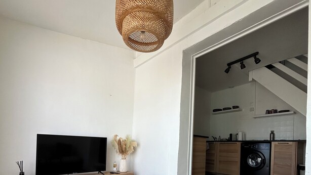 A modern living room with a flat-screen TV, wooden entertainment unit, and a woven pendant light.