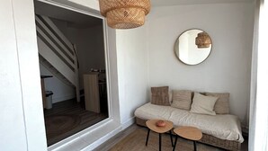 Tunnelmallinen olohuone, jossa on sohva, kaksi pientä pöytää, punottu lattiavalaisin ja pyöreä peili seinällä.