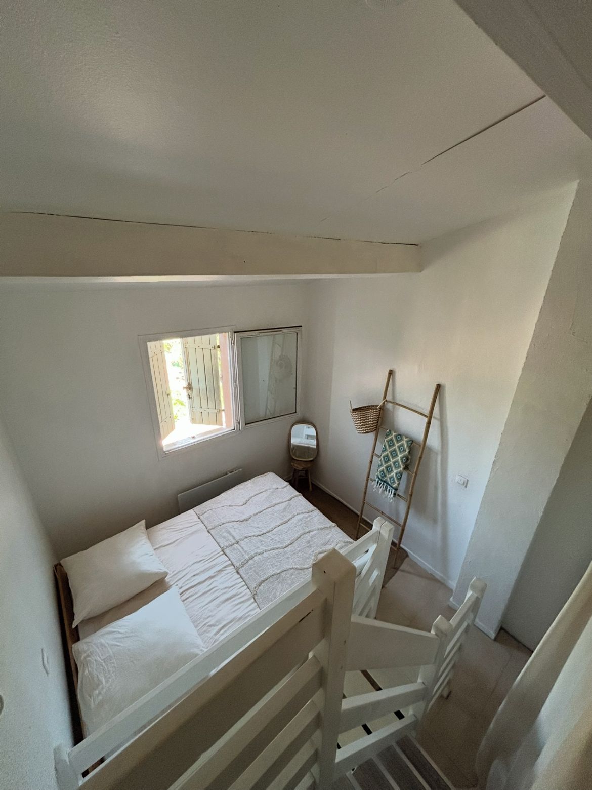 A small, single-bed room with a sloped ceiling, a window, a bedside table, and a chair.