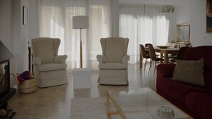 Een woonkamer met twee fauteuils, een rode bank, een glazen salontafel en een eethoek op de achtergrond.