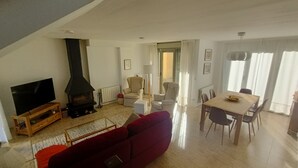 Een woonkamer met een televisie, open haard, rode bank, eettafel en stoelen.