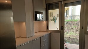 Een moderne keuken met witte kasten, een ingebouwde magnetron en een schuifdeur naar een terras.