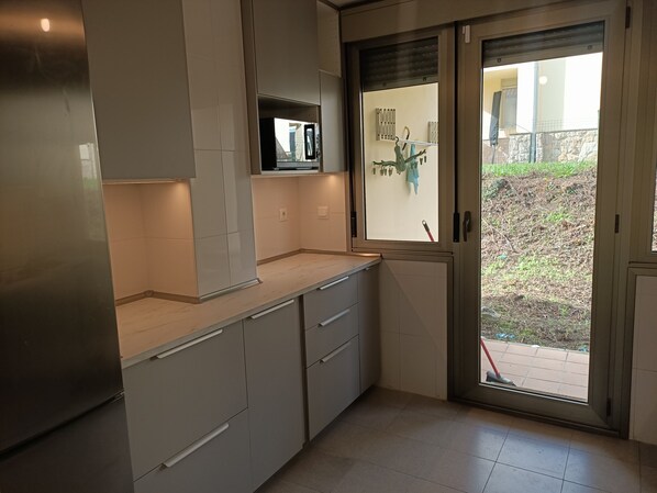 A modern kitchen with white cabinets, a built-in microwave, and a sliding glass door leading to a patio.