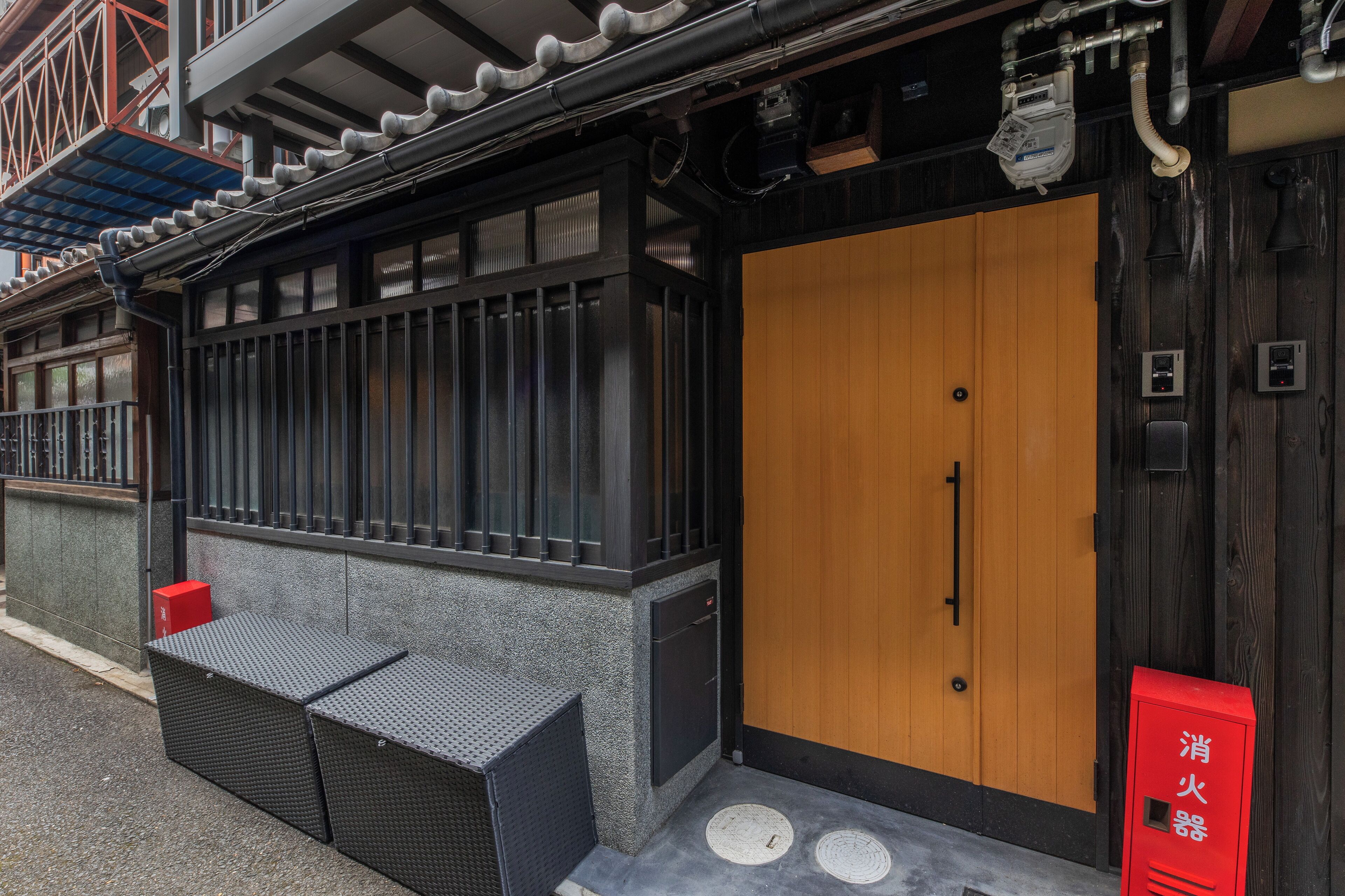 A traditional Japanese building with a wooden door, a small outdoor seating area, and a red mailbox.