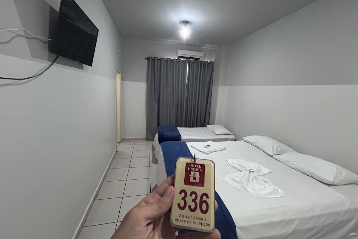 A hotel room with two beds, a TV mounted on the wall, and a ceiling light.