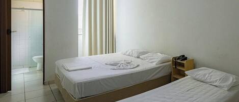 A hotel room with two beds, a wooden nightstand, a telephone, and a window with curtains.