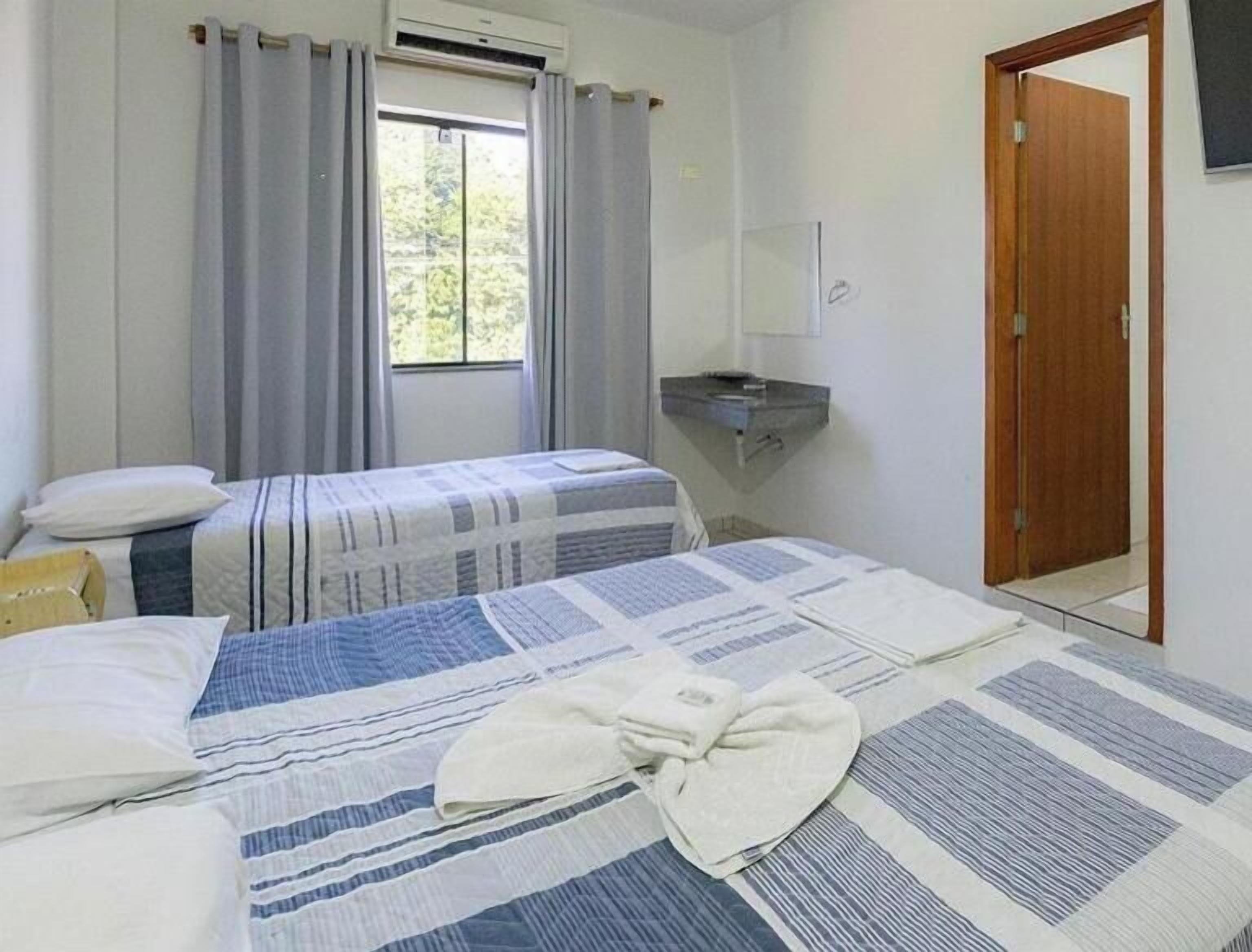A simple room with two beds, a window with curtains, a small sink, and a mirror.