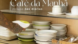 A kitchen area with stacked plates and bowls, and a person reaching for a bowl. - Hotel Palace Huesca (Presidente Prudente)