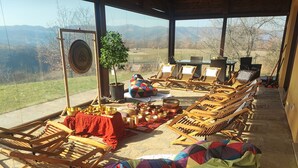 A room with a view of mountains, wooden lounge chairs, a table with bowls, and a colorful bean bag.