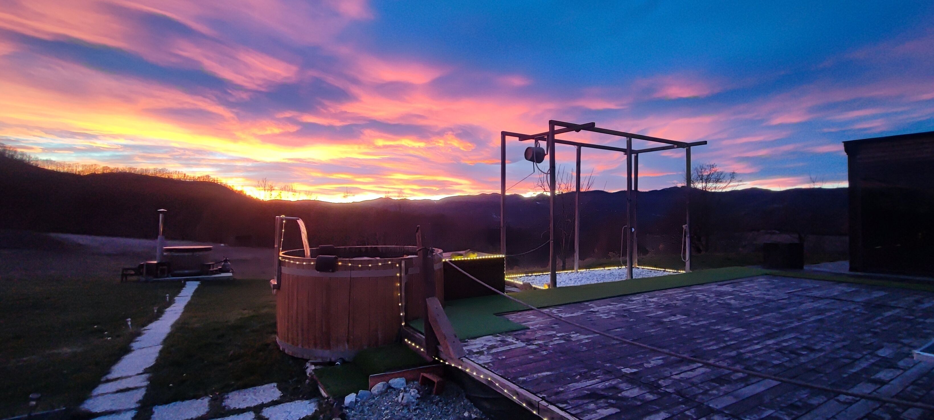 Une terrasse en bois avec un jacuzzi et une balançoire, le tout baigné par les couleurs d’un coucher de soleil.