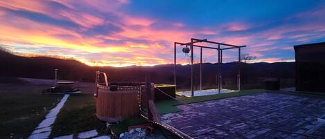 Une terrasse en bois avec un jacuzzi et une balançoire, le tout baigné par les couleurs d’un coucher de soleil.