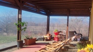 Un espacio de descanso al aire libre con sillones de madera, plantas en macetas y un jarrón grande con flores.