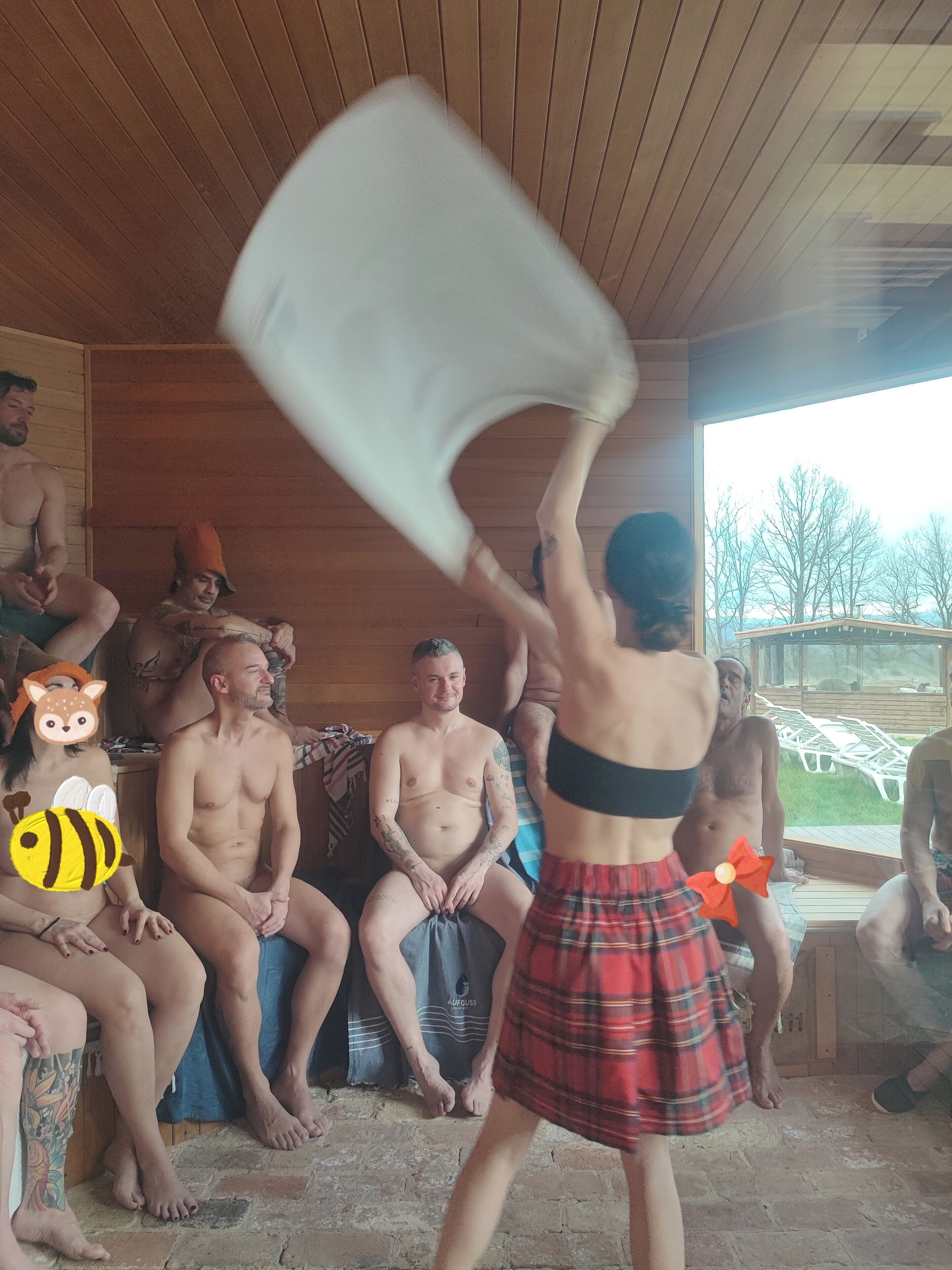 A group of people in a wooden cabin with a large window, a wooden ceiling, and a stone floor.