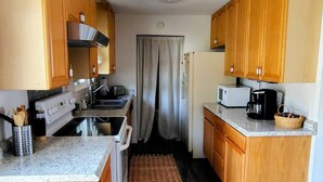Una cocina compacta con armarios de madera, microondas, estufa y cafetera.