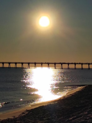 Um cais se estende por águas calmas, com o sol refletindo em sua superfície.