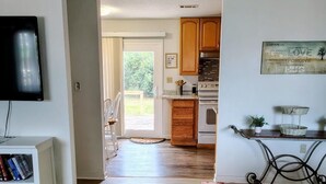 Amplia sala de estar con televisión, una estantería y un comedor con muebles de madera y una cocina al fondo.