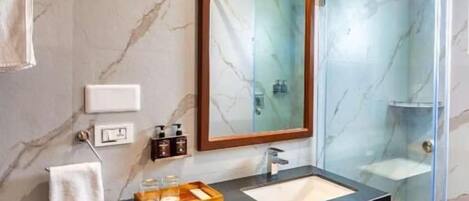 Un baño moderno con pared de mármol, tocador de madera, cabina de ducha de vidrio y un espejo grande.