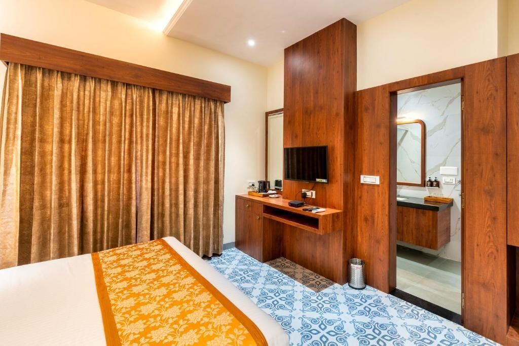Une chambre d’hôtel avec un lit, un bureau en bois, un miroir et une salle de bain visible à travers une porte ouverte.