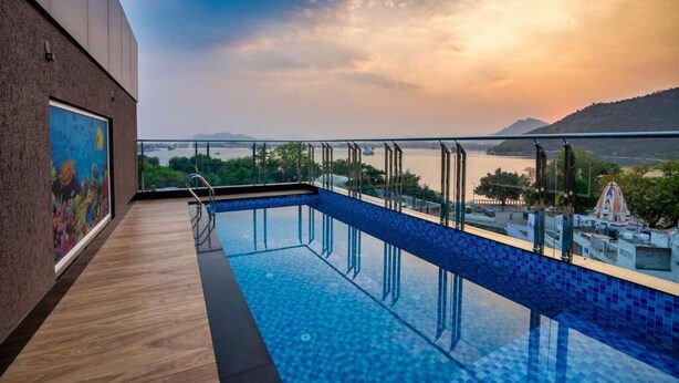 A rooftop infinity pool with a glass barrier, wooden deck, and a mural on the adjacent wall. - The Grand Fateh (Udaipur)