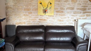 Una stanza con parete in pietra, un divano in pelle nera, soffitto in legno e un'opera d'arte gialla.