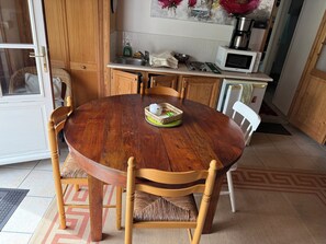 Une table à manger en bois avec des chaises, un coin cuisine équipé d’un four à micro-ondes et un panier posé sur la table.