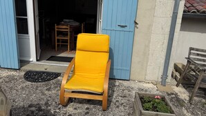 Una poltrona da lounge in legno con cuscino, una porta blu e una piccola zona giardino con piante.