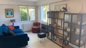 A living room with a blue sofa, a red armchair, a black side table, and a bookshelf filled with books and decorative items.