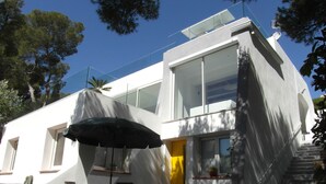 A modern two-story house with large windows, a staircase, and a covered outdoor seating area.