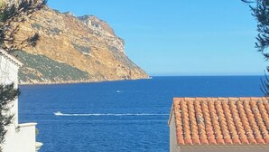 A coastal view with a rocky cliff, a clear blue sea, and a tiled-roof building.