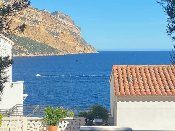 A coastal view with a rocky cliff, a clear blue sea, and a tiled-roof building.