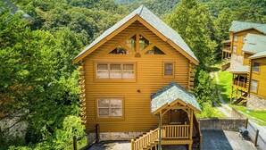 A wooden cabin with a porch and a staircase, surrounded by lush greenery and mountains in the background. - Panoramic View-Pigeon Forge Two Bedroom Plus Loft Cabin Rental-Swimming Pool (Sevierville)