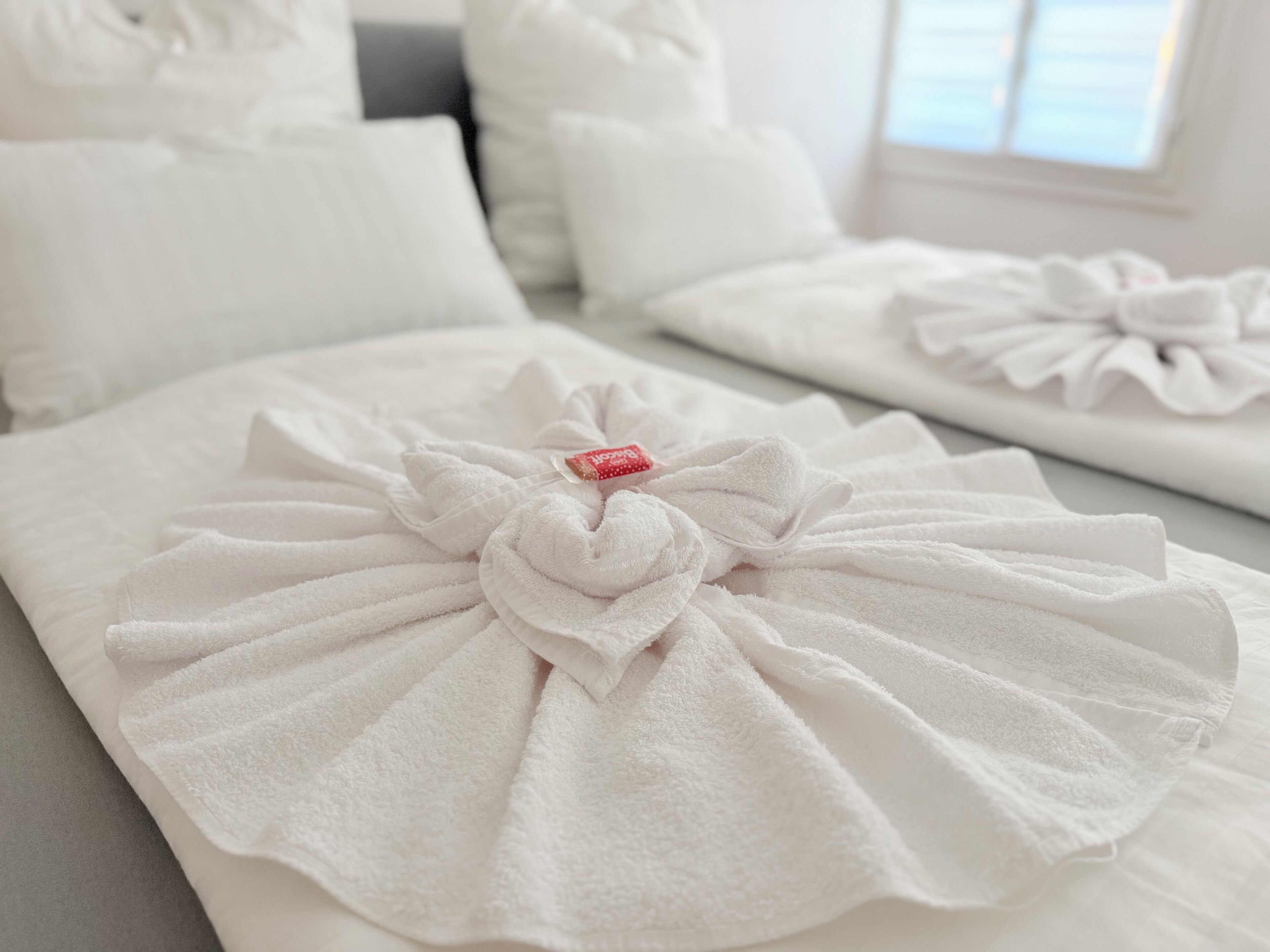 Habitación de hotel impecable con toallas blancas dobladas en formas decorativas sobre la cama.