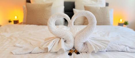 Una cama con una toalla dispuesta en forma de corazón y dos velas a cada lado.