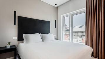A modern hotel room with a large bed, a small bedside table, and a window with curtains.