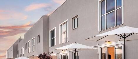 Un edificio moderno con fachada gris, ventanas amplias y zona de estar exterior con sombrillas.