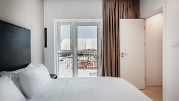 A hotel room with a bed, a door, and a view of a balcony with plants.