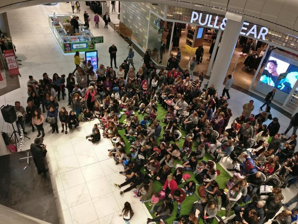 Un espacio interior concurrido donde varias personas se reúnen alrededor de un área central, posiblemente un escenario o punto de interés.