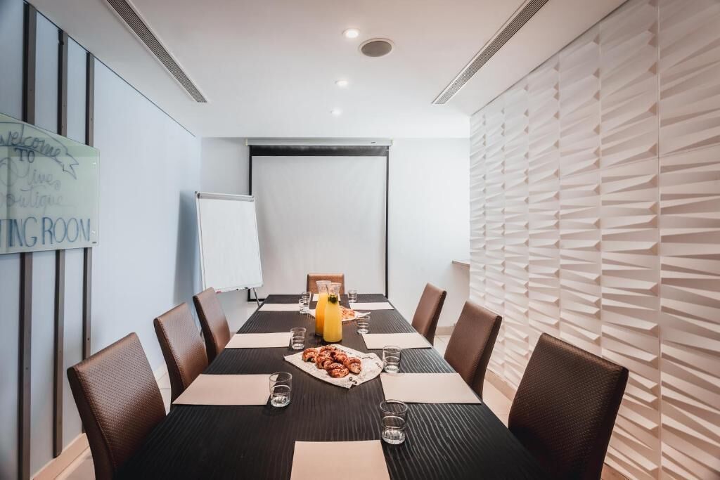 Une salle de conférence avec une longue table, des chaises marron, un écran de projection et un tableau blanc.