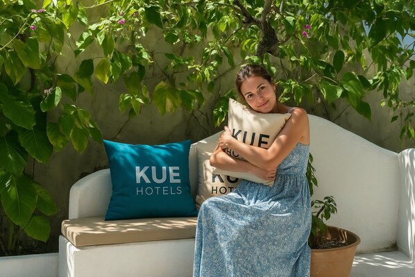 Una persona sentada en un sofá blanco con un cojín que dice "KUE HOTELS".