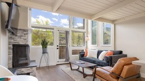 A living room with a fireplace, a sofa, a coffee table, and a TV. - Modern Condo with Vail Mountain Views (Vail)