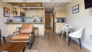 A compact living space with a kitchenette, a dining area with a leather chair, and a small white table. - Modern Condo with Vail Mountain Views (Vail)