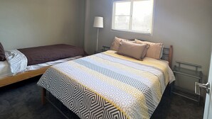Une chambre à coucher avec un lit, une fenêtre avec des stores, un ventilateur de plafond et un luminaire.