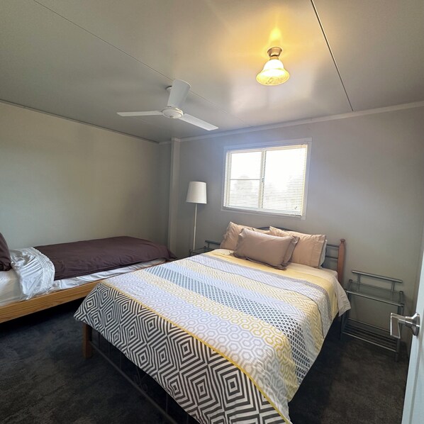 Ein Schlafzimmer mit einem Bett, einem Fenster mit Jalousien, einem Deckenventilator und einer Lampenleuchte.